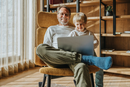Smiling boy using laptop while sitting with father on chair