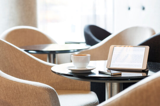 Digital tablet, smartphone and cup of coffee on table in hotel lobby