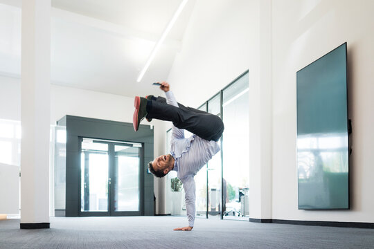 Businessman with cell phone doing a one-handed handstand on office floor