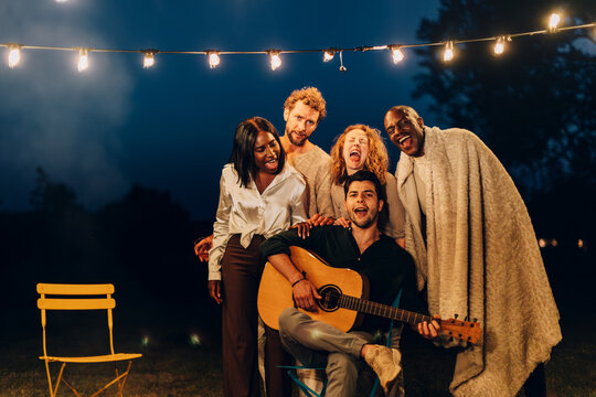 Diverse friends singing and playing guitar enjoying outdoor party at night