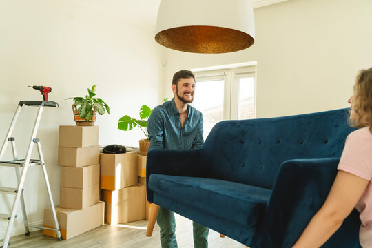 Smiling man carrying sofa with help of girlfriend at home