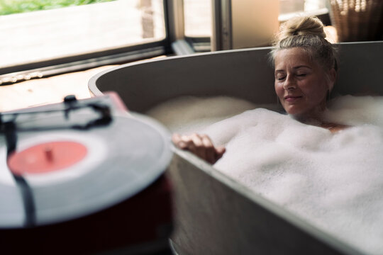 Mature woman taking bubble bath, listening music from analogue record player
