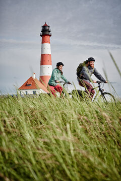 Germany, Schleswig-Holstein, Eiderstedt, couple riding bicycle near Westerheversand Lighthouse