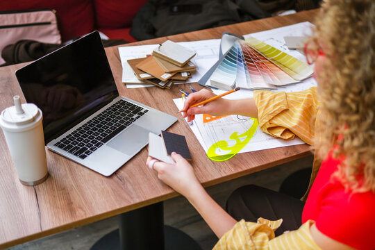 Interior designer working on blueprint at desk with laptop