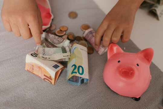 Hands counting saved money next to a pink piggy bank