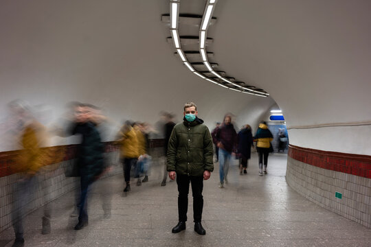 Young man with face mask standing isolated in subway underpass, with people moving around him