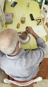 Abuelo desayunando taza de caf&eacute; dar vueltas cuchara viejo calvo aud&iacute;fono mesa cocina casa tercera edad desayuno, having breakfast old man spin around with spoon, despertar mayor morning ma&ntilde;ana cenital