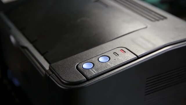 Close up on black laser printer, showing control panel with two glowing blue buttons and status indicator lamps, essential equipment for daily tasks in office or home setting