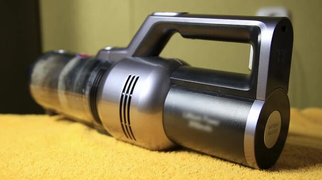 Close up view of contemporary cordless vacuum cleaner, highlighting its ergonomic handle, metallic grey finish, and black accents, showing charged battery on digital screen, prepared for household cle