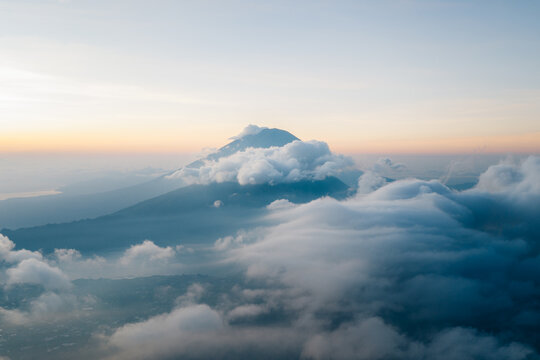 Aerial view of Mount Batur surrounded by thick clouds at sunrise, with the volcanic peak rising above the mist in Kintamani, Bali, Indonesia.