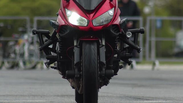 Close up front view of red sports motorcycle with specialized crash bars for stunt riding. Motorcycle performs dynamic wheelie, front tire off ground, demonstrating extreme control. Performance on asp