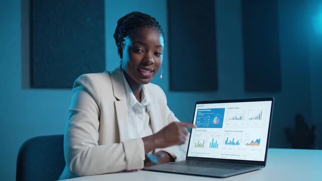 A professional woman presents data insights using a laptop in a modern setting, showcasing colorful graphs and statistics for analysis and decision-making.