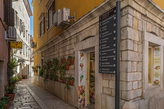 Poreč, Croatia - June 8, 2022: Small street with street signs marking the direction to the restaurants, shops and sites to visit in city. Poreč, 2000 years old, is a town on the Istrian peninsula.