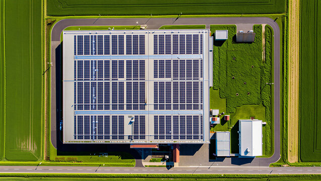 Aerial view of an industrial building with rooftop solar panels surrounded by green fields