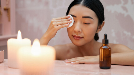 Fototapeta premium Young Asian woman removing makeup with cotton pad by candles 