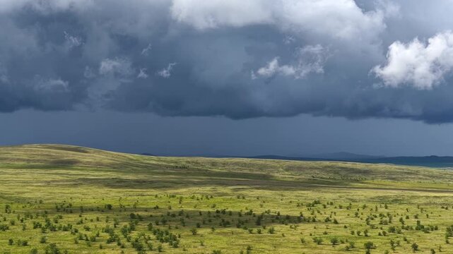 Dramatic cinematic drone shot of an endless steppe landscape under a dark, stormy sky before a thunderstorm. Open field landscape from above