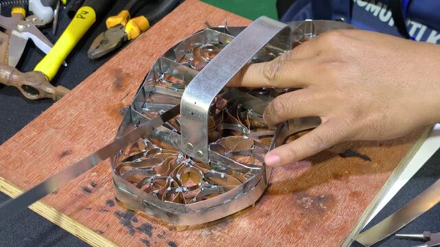 A craftsman creates a copper batik stamp. This traditional Malay art tool is dipped in hot wax to stamp patterns onto fabric. It saves time compared to hand-drawing.