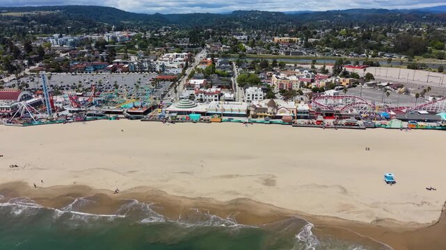 Aerial drone view of the Santa Cruz Beach Boardwalk amusement park with ocean waves rolling onto a sandy beach.