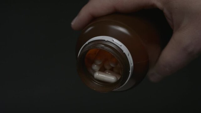 Capsules spilling from a brown prescription bottle in slow motion. Studio close-up with black background and pharmaceutical concept.
