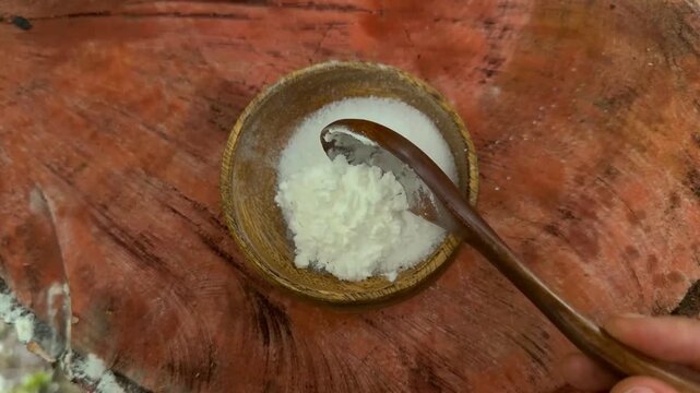 A culinary expert combines white starch with water in a wooden bowl, stirring the mixture thoroughly with a wooden spoon to form a smooth thickening agent for cooking various rich sauces outdoors.