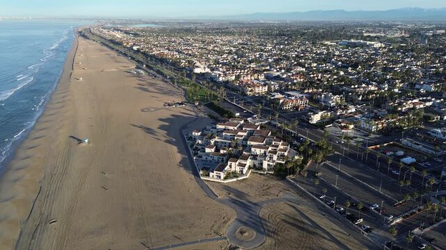 Coastal Urban Panorama captures Huntington Beach developments lush palms bordering expansive sandy shoreline. Morning shadows stretch across beach, highlighting urban life in Orange County, CA