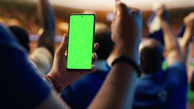 Close up of isolated screen mobile phone used by soccer fan to compare match odds, cheering in stadium, showing football supporter checking live score app predictions on chroma key smartphone.