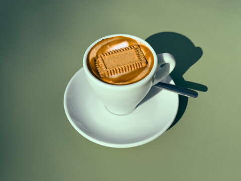 Still life of cookie floating on top of espresso in cup on saucer against green background