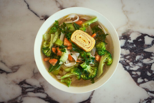 View from above of chicken broth with tamago and vegetables in bowl on marbled countertop