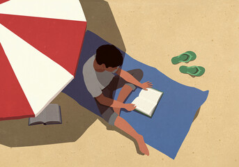 High angle view young man reading book in shade under striped umbrella on sunny summer beach