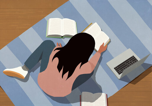 Teenage girl studying, reading books next to laptop on striped rug