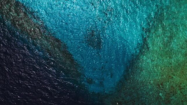 Aerial top down view of a Maldives resort lagoon and coral reef, with a wooden overwater villa platform at right and a small floating object near center in midday sun