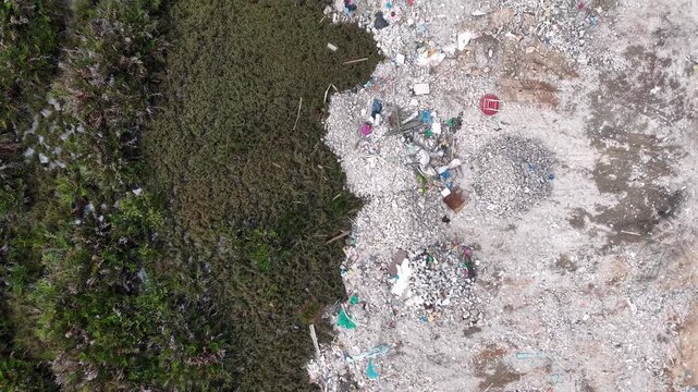 Drone aerial view showing outdoor rubbish dump adjacent to marsh vegetation and scattered construction debris.