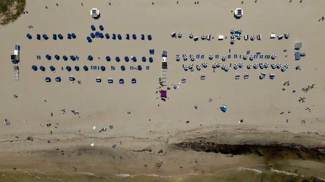Aerial view of South Beach featuring rows of blue and white beach umbrellas and lounge chairs on the sand in Miami Beach, Florida, United States.