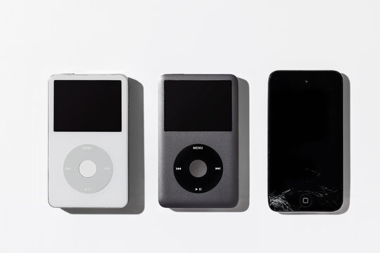 Bangkok, Thailand - May 3, 2026: Top view of classic iPod and a cracked screen multimedia device on a white surface. Nostalgic retro technology concept.