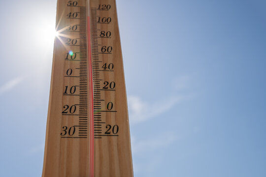 Wooden Thermometer Showing High Temperature in Bright Sunlight Against Blue Summer Sky