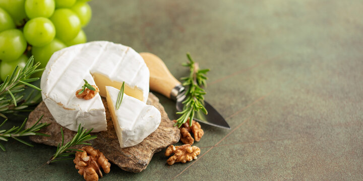Soft brie or camembert cheese on a stone board, chine muscat grapes, walnut and rosemary branches on a green background