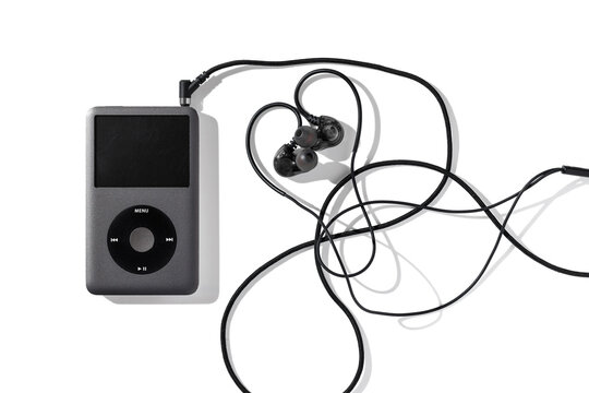 Bangkok, Thailand - May 3, 2026: A vintage Grey Apple iPod Classic music player with professional black in-ear monitors on a white surface.