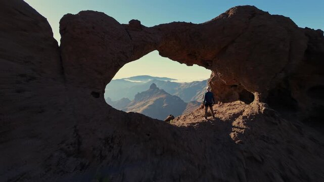 Aerial view revealing a hiker standing at the impressive Aserrador Arch, a natural rock formation in Gran Canaria, Canary Islands, Spain