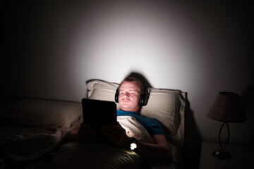 Fototapeta premium Man watching tablet in bed at night suffering insomnia