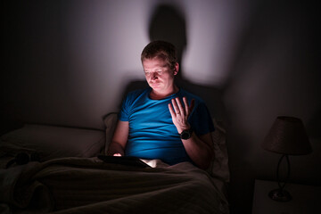 Fototapeta premium Man experiencing insomnia using tablet in dark bedroom