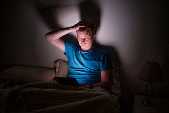 Stressed man looking at tablet in bed struggle with insomnia