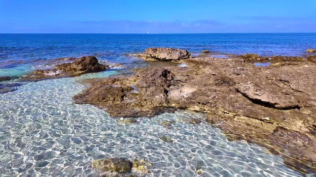 Crystal clear shallow water and rocky coastline at Is Arutas beach in Sardinia, Italy. Transparent turquoise sea with sun ripples on the sandy bottom under a clear blue sky