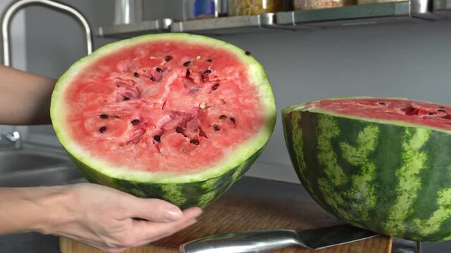 A close-up of a large watermelon, cut in half, being held by a woman. An unidentified woman is showing an overripe watermelon, cut in half.