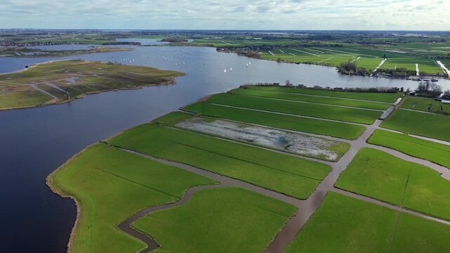 Aerial view of a historic windmill, polder canals, and sailboats. Drone landscape of green meadows, wide agricultural waterways, and sailing yachts in the Netherlands countryside, panorama.