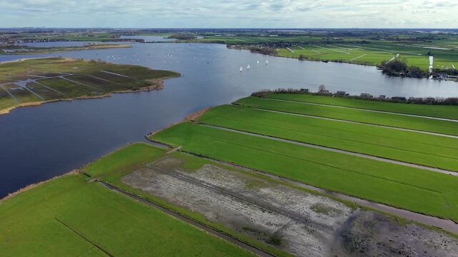 Aerial view of a historic windmill, green polder fields, and sailboats. Drone landscape of wide agricultural canals, lakes, and sailing yachts in the Netherlands countryside, panorama.