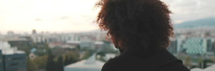 Obraz premium Close-up of young guy is standing on the balcony looking at the city, back view. Panoramic