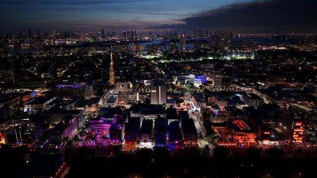 Aerial view of South Beach at night, featuring illuminated art deco buildings, vibrant neon lights along the streets, and the distant skyline of Miami Beach, Florida, United States.