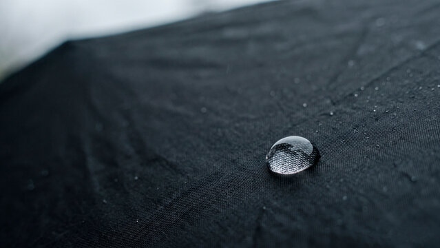 Single water droplet on dark waterproof fabric, concept of water resistance and protection from rainy weather