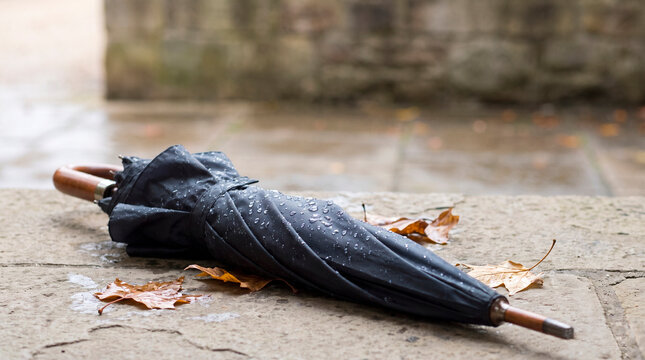 Closed umbrella covered with raindrops on a stone ledge, concept of rainy weather and everyday urban resilience