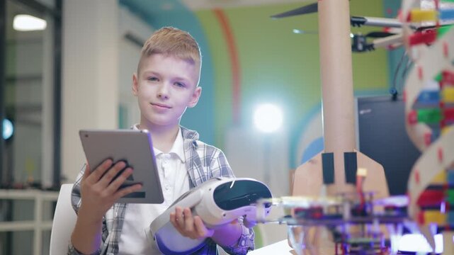 Boy piloting drone with tablet computer in makerspace workshop while holding vr controller and prototype.